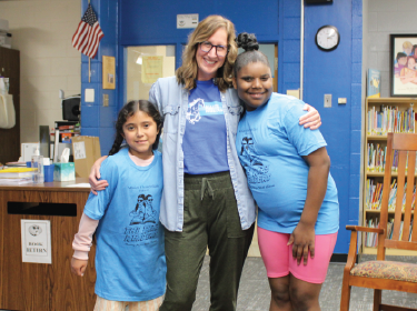 teacher wrapping arms around two students